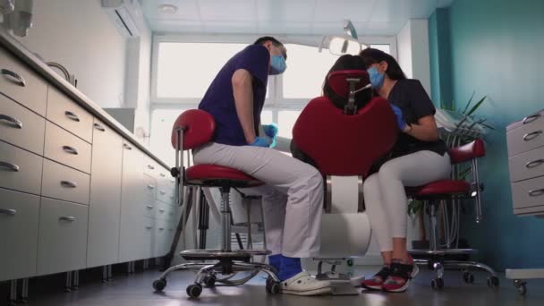 Médicos dentistas mujer y hombre en máscaras médicas atienden paciente en clínica dental - Metraje, vídeo