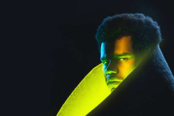アフリカ系アメリカ人の若い男の肖像画暗い背景にネオン黄色の輝き. - 写真・画像