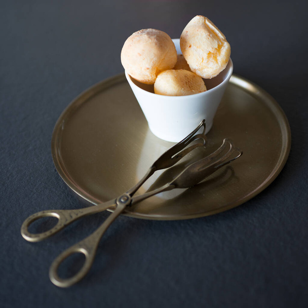 Delicious bite dessert filled with cream. Set in a white bowl on an antique bronze tray. Beautiful bronze serving tongs. Black background. - Fotó, kép