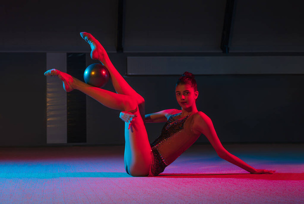 Giovane ragazza graziosa ginnasta ritmica isolato su sfondo scuro in luce al neon - Foto, immagini