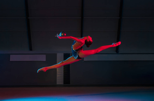 Jovem graciosa menina ginasta rítmica isolado no fundo escuro em luz de néon - Foto, Imagem