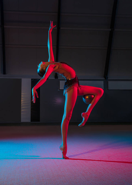 Молода витончена дівчина ритмічна гімнастка ізольована на темному фоні в неоновому світлі
 - Фото, зображення