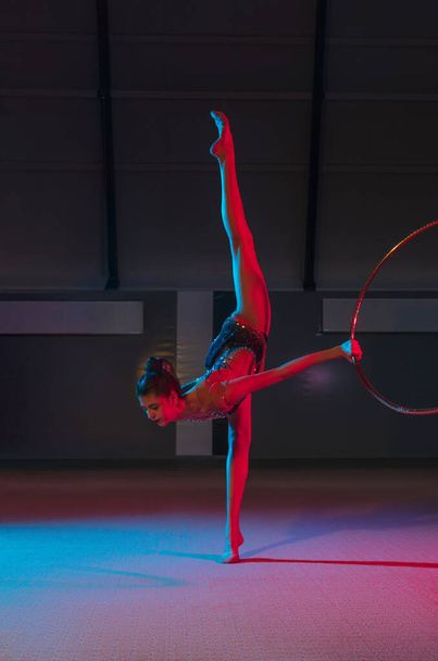Young graceful girl rhythmic gymnast isolated on dark background in neon light - Photo, Image