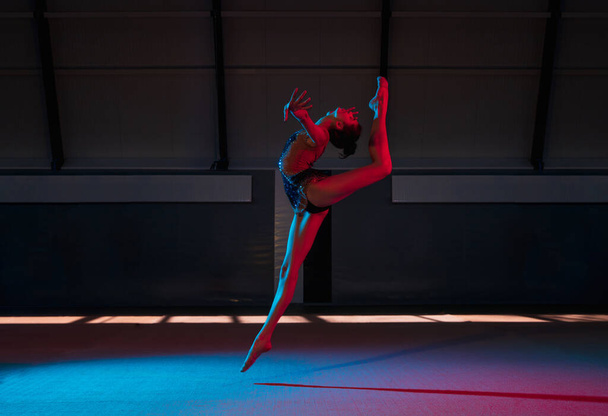 Jeune fille gracieuse gymnaste rythmique isolé sur fond sombre dans la lumière au néon - Photo, image