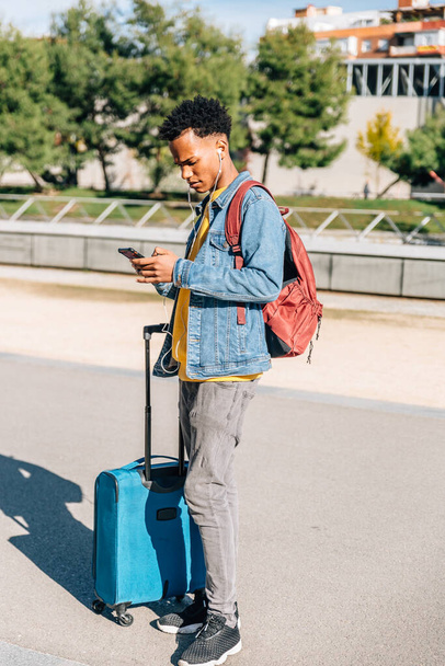 Afro hombre viajero pelo comprueba su teléfono móvil en una ciudad en un día soleado - Foto, imagen
