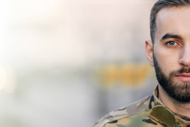 metade do rosto de um soldado masculino em uniforme de camuflagem com barba e olhos tristes. - Foto, Imagem