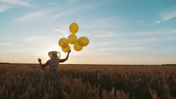 Vrouw met ballonnen in de hand loopt door een tarweveld bij zonsondergang - Video