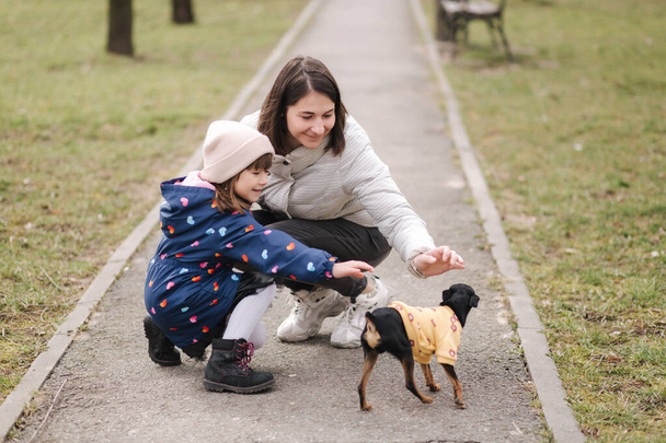 Красивая молодая мама гуляет с дочерью и собачкой. Счастливая семья гуляет с домашними животными во время карантина - Фото, изображение