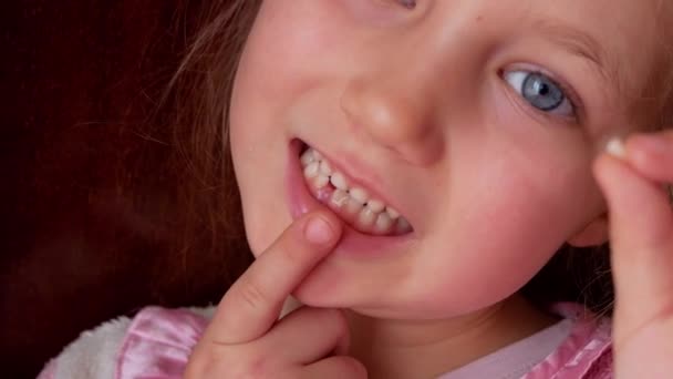 Schattig kleuter kind wiebelen haar lagere melktand en glimlachen. Vrome tand vervanging door permanente 4k beeldmateriaal donkere achtergrond. Bang klein meisje 6-7 jaar oud heeft snijtand verloren. - Video