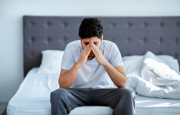 Мужская депрессия. Несчастный араб сидит на кровати и думает о проблемах, закрывая лицо руками - Фото, изображение