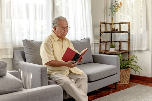 Starszy Azjata czyta książkę i zostaje sam w domu. Styl życia w wieku emerytalnym. - Zdjęcie, obraz