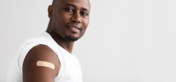 Coronavirus immunisatie. Positieve zwarte man toont zijn arm met een lijmverband panorama met vrije ruimte - Foto, afbeelding