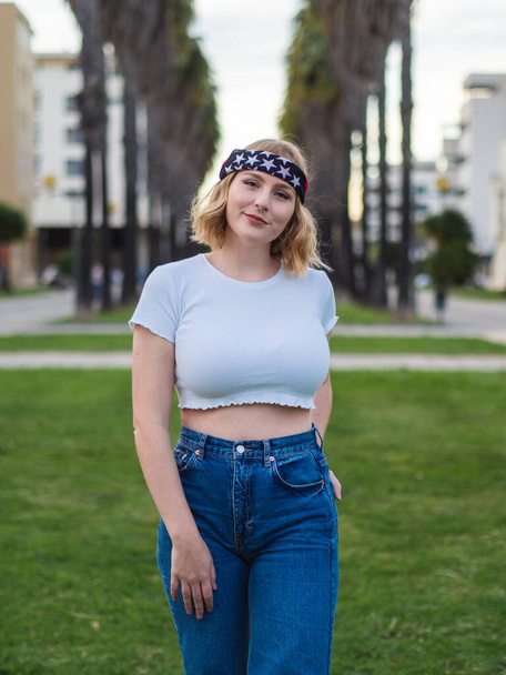 A shallow focus of a beautiful Caucasian woman in a trendy bandana and crop top posing at a park - Foto, immagini