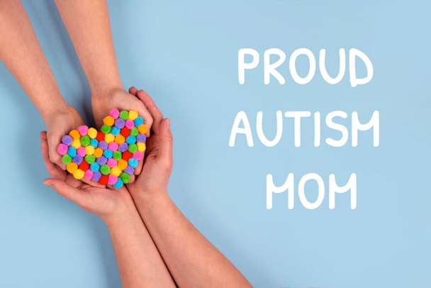 Stolze Autismus-Mutter und World Autism Awareness Day Konzept - autistische Kinderhände unterstützt von einer Mutter, die ein buntes Herz auf blauem Hintergrund hält. Autismus-Spektrum-Störung. Selektiver Fokus - Foto, Bild