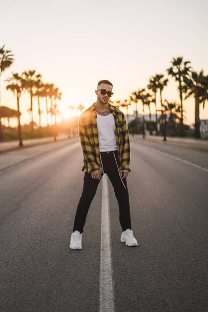 A vertical shot of a stylish European man standing on a road at sunset - Фото, изображение
