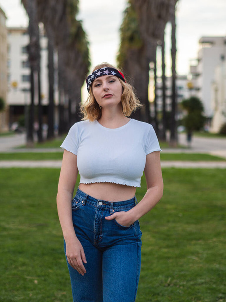 A shallow focus of a beautiful Caucasian woman in a trendy bandana and crop top posing at a park - Foto, Imagem