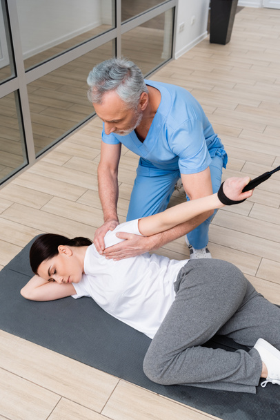 fizikoterapeuta segít a nőnek edzeni a fitnesz szőnyegen a kórházban tornaterem - Fotó, kép