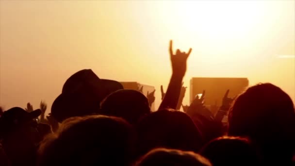 Силуэты заднего вида людей с поднятыми руками против освещаемых черными огнями сцены во время музыкального исполнения - Кадры, видео