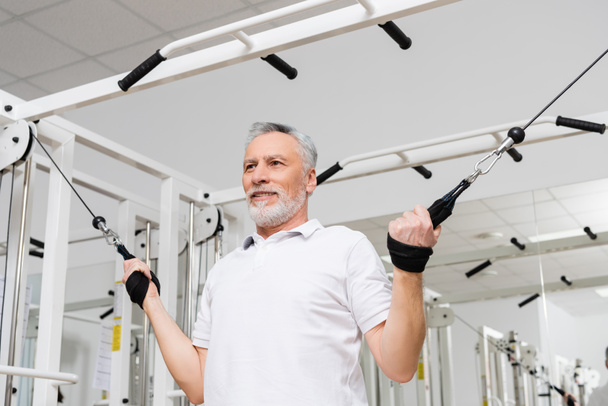 улыбающийся мужчина тренируется в больничном спортзале во время физической реабилитации - Фото, изображение