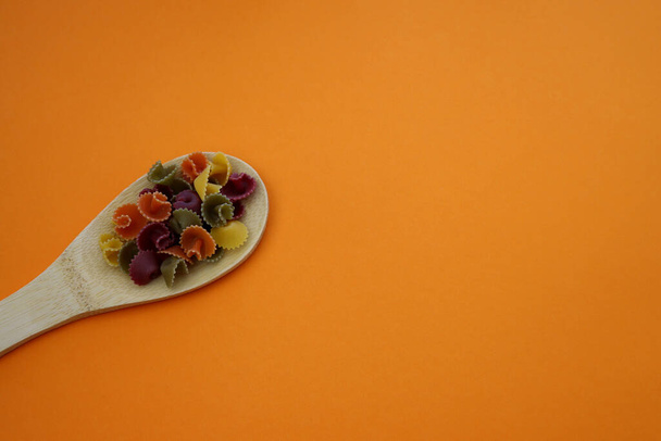 Wielokolorowy makaron margarita w drewnianej łyżce na pomarańczowym tle. - Zdjęcie, obraz