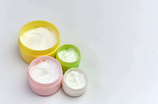 Набор открытых разноцветных банок с белым косметическим кремом для лица и тела на белом фоне, - Фото, изображение