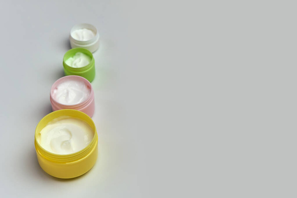 Set de frascos multicolores abiertos con crema cosmética blanca para la cara y el cuerpo sobre un fondo blanco, - Foto, Imagen