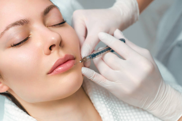 Ajaknagyobbító és -javító eljárás kozmetikai szalonban. A szakorvos beadja az injekciót a beteg ajkába.. - Fotó, kép