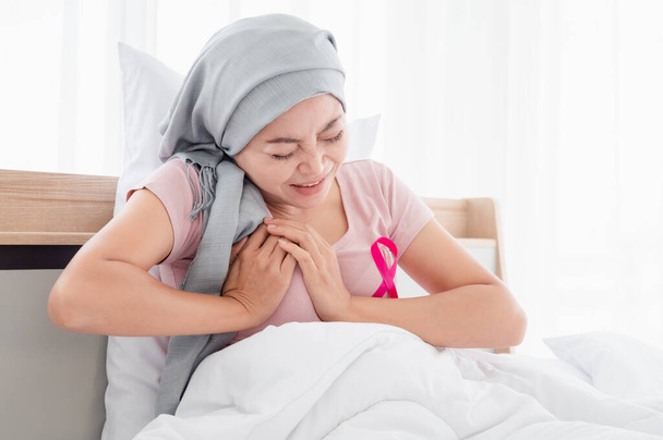 Fiatal ázsiai nők hidzsábot viselnek, kézen fogva a mellkasukat, fájdalom miatt, miközben az ágyban ülnek. Emlőrák utáni felépülést jelez Emlőrák koncepció, rákmegelőzés koncepció. - Fotó, kép