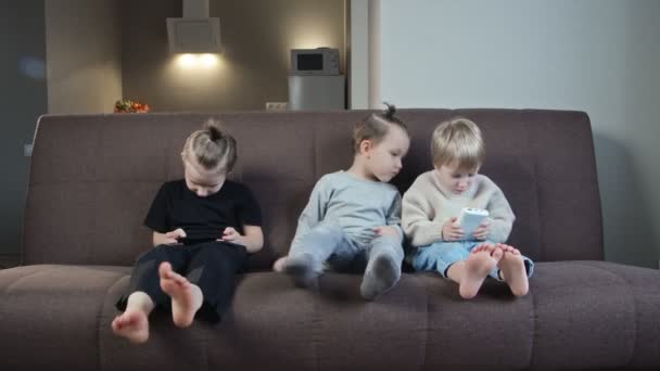 Les enfants jouent avec des gadgets. Jouez à des jeux en ligne à la maison sur le canapé. Les parents contrôlent les enfants - Séquence, vidéo