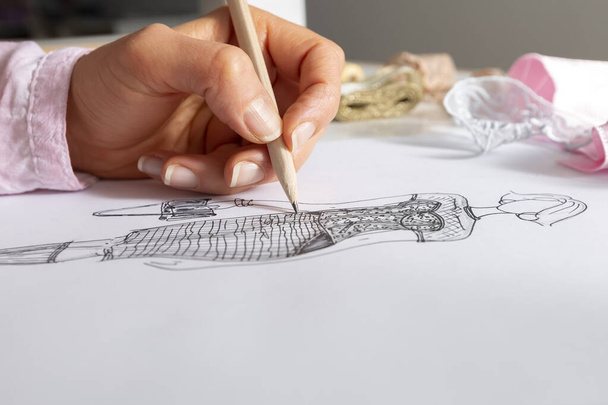 The designer draws sketches of fashionable women's clothing on paper at the workplace. - Фото, изображение