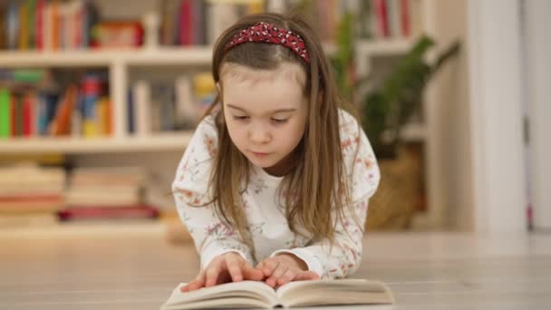Skupiona mała dziewczynka czyta książkę w domu - Materiał filmowy, wideo