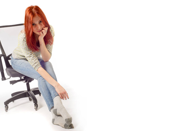 Ofis koltuğunda oturan, kot pantolonlu kızıl saçlı kız. - Fotoğraf, Görsel