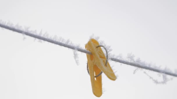 Pinzas de tela multicolores en una cuerda en escarcha cuelgan de una cuerda en el invierno afuera en la nieve - Imágenes, Vídeo