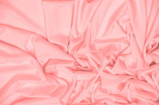 The fabric is silk of a pale red color. Texture. Background. Pattern. Silk fabric has a shiny sheen and characteristic small folds that run horizontally. She lies down in soft folds - Photo, image