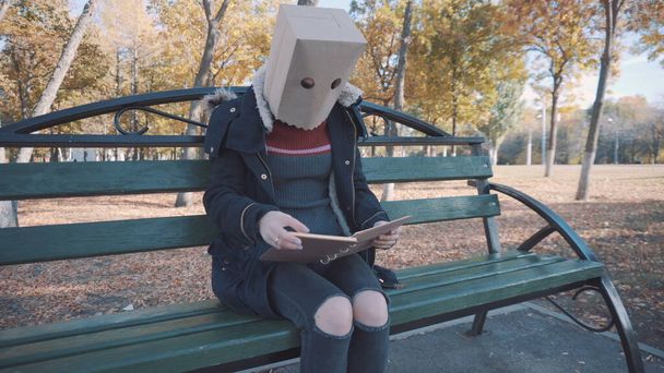 Το κορίτσι με το πακέτο στο κεφάλι κάθεται σε ένα παγκάκι και διαβάζει ένα βιβλίο. Κορίτσι με σακάκι. - Φωτογραφία, εικόνα