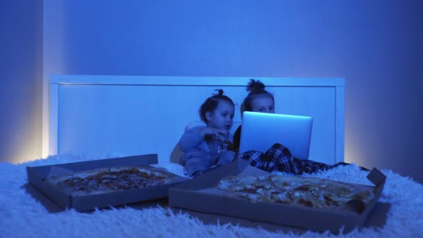Zwei kleine Jungen liegen im Bett, schauen sich einen Film auf dem Notizbuch an und essen nachts Pizza - Filmmaterial, Video