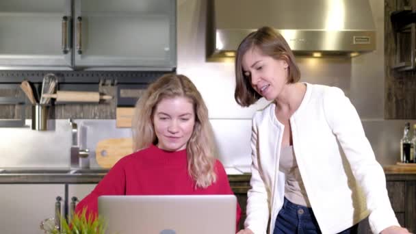 İki kız uzaktan evde birlikte çalışıyor. İş kadınları iş projelerini mutfaktaki bilgisayarda tartışırlar. Fikir alışverişi ve beyin fırtınası. Tartışma ve karar. Çalışan profesyonellerden oluşan bir ekip - Video, Çekim