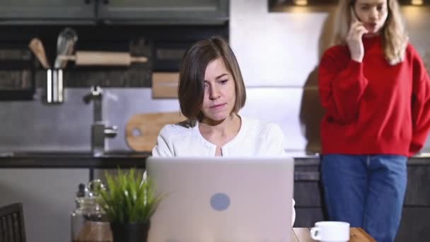 Two beautiful young girls are working in kitchen home with laptop. Female freelancers work home during quarantine. girl is sitting at table and typing. Home office in the kitchen. online business. - Footage, Video