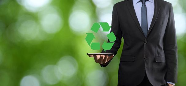 Businessman in suit over natural green background holds an recycling icon, sign in his hands. Ecology, environment and conservation concept. - Photo, Image