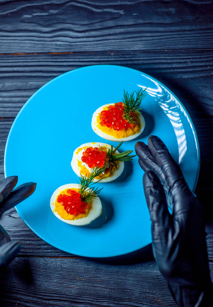Eggs with red caviar on a blue plate serving in black gloves serving restaurant - Photo, Image