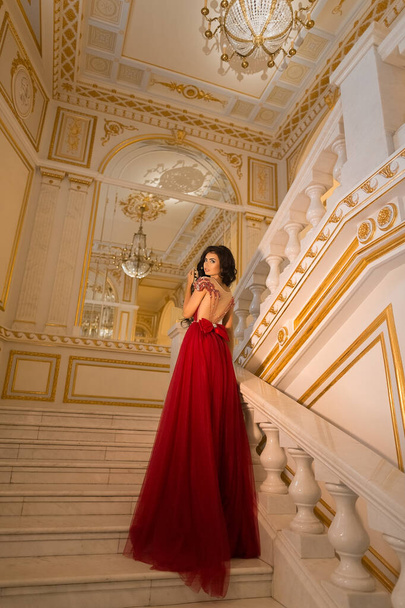Bella ragazza bruna in un abito da ballo rosso sullo sfondo degli interni del palazzo bianco e oro - Foto, immagini