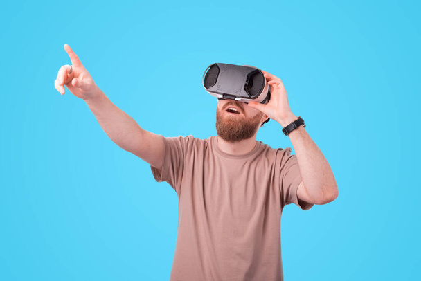 Jeune homme barbu pointant du doigt et portant des lunettes VR, Expérience de réalité virtuelle. - Photo, image