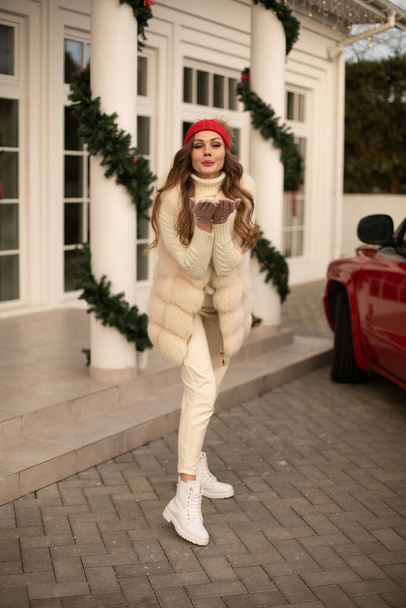 白い毛皮のコートと赤い帽子の魅力的な女性は外で笑顔とカメラにポーズ - 写真・画像