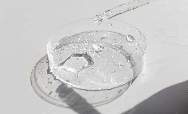 Прозрачный жидкий гель или гиалуроновая сывороточная кислота в чашке Петри с пипеткой. Концепция гидратации и ухода за кожей - Фото, изображение