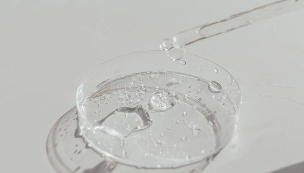 Transparante vloeibare gel of hyaluronzuur in petrischaaltje met pipet. Hydraterende en huidverzorgingsconcept - Foto, afbeelding