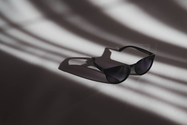 Stylové černé sluneční brýle na bílém pozadí se stíny. Plastové brýle s přechodem na slunný den. - Fotografie, Obrázek