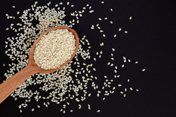 White sesame seeds in wooden spoon on pile of white sesame seeds, top view. - Photo, Image