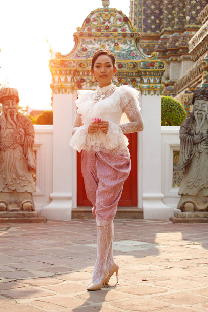 Beautiful Asian Woman in Thai Traditional Costume which is very Elite and old Fashion. Lady in Public area Wat Temple with retro architecture for travel tourism. copy space background - Photo, Image