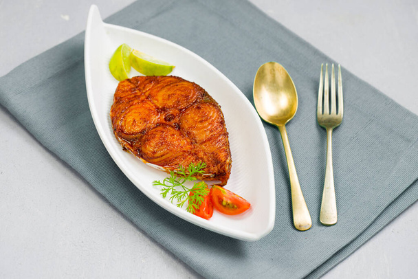 Seer ryby smažené uspořádány krásně a zdobené cibulí, citronem a rajčaty plátky na bílém keramickém talíři umístěny na světle zelený odstín ubrousky s šedou texturou pozadí. - Fotografie, Obrázek