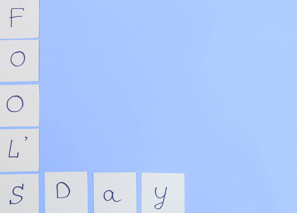 Ручная записка на бумажный день дураков слева на синем фоне с местом для текста справа, вид сверху крупным планом. - Фото, изображение